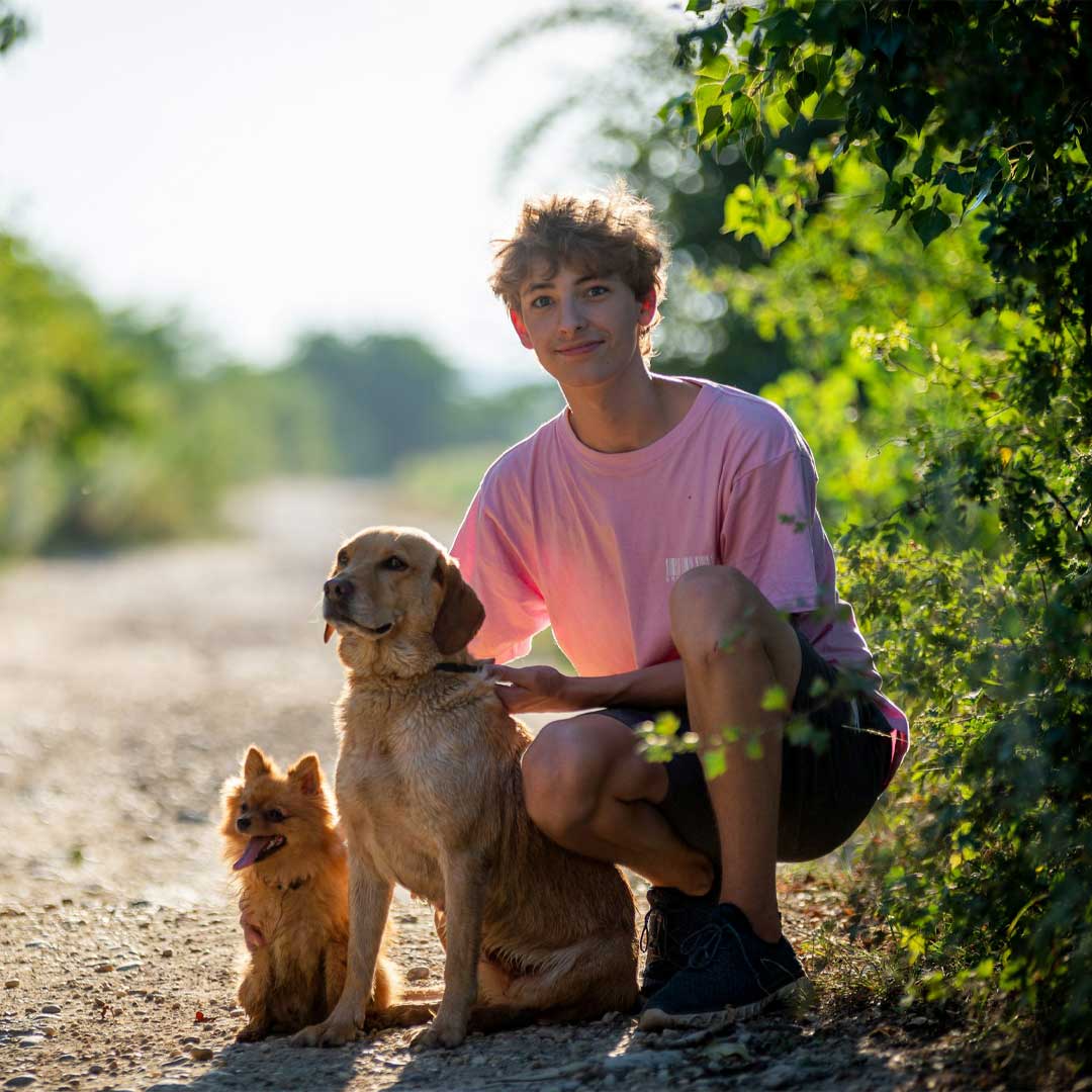 A-body-with-his-two-dogs-out-in-a-farm-road A body with his two dogs one big and one small, out in a farm road with a beautiful green view at the back